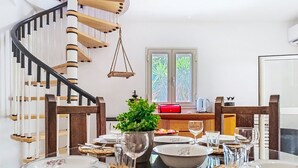 A dining area with a spiral staircase, a window with a view of greenery, and a table set for a meal. - Casa Paolina by Interhome (Modica)