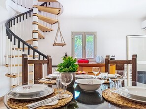 Un coin repas agrémenté d’un escalier en colimaçon, d’une fenêtre donnant sur un paysage verdoyant et d’une table mise pour le repas.