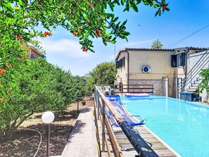 A swimming pool with a wooden deck, a covered area, and a building with a staircase.