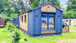 A modern, single-story cabin with a large glass door and windows, surrounded by lush greenery.