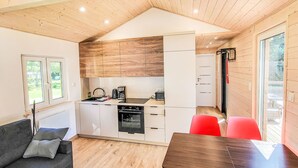 A compact kitchen with wooden cabinets, a built-in oven, and a dining area with a table and red chairs.