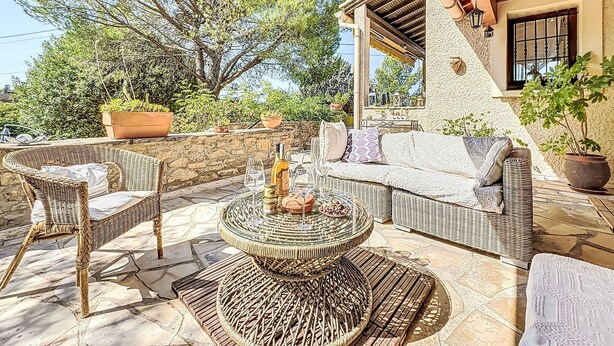 Une terrasse extérieure aménagée avec des meubles en osier, une table ronde et des plantes en pot.