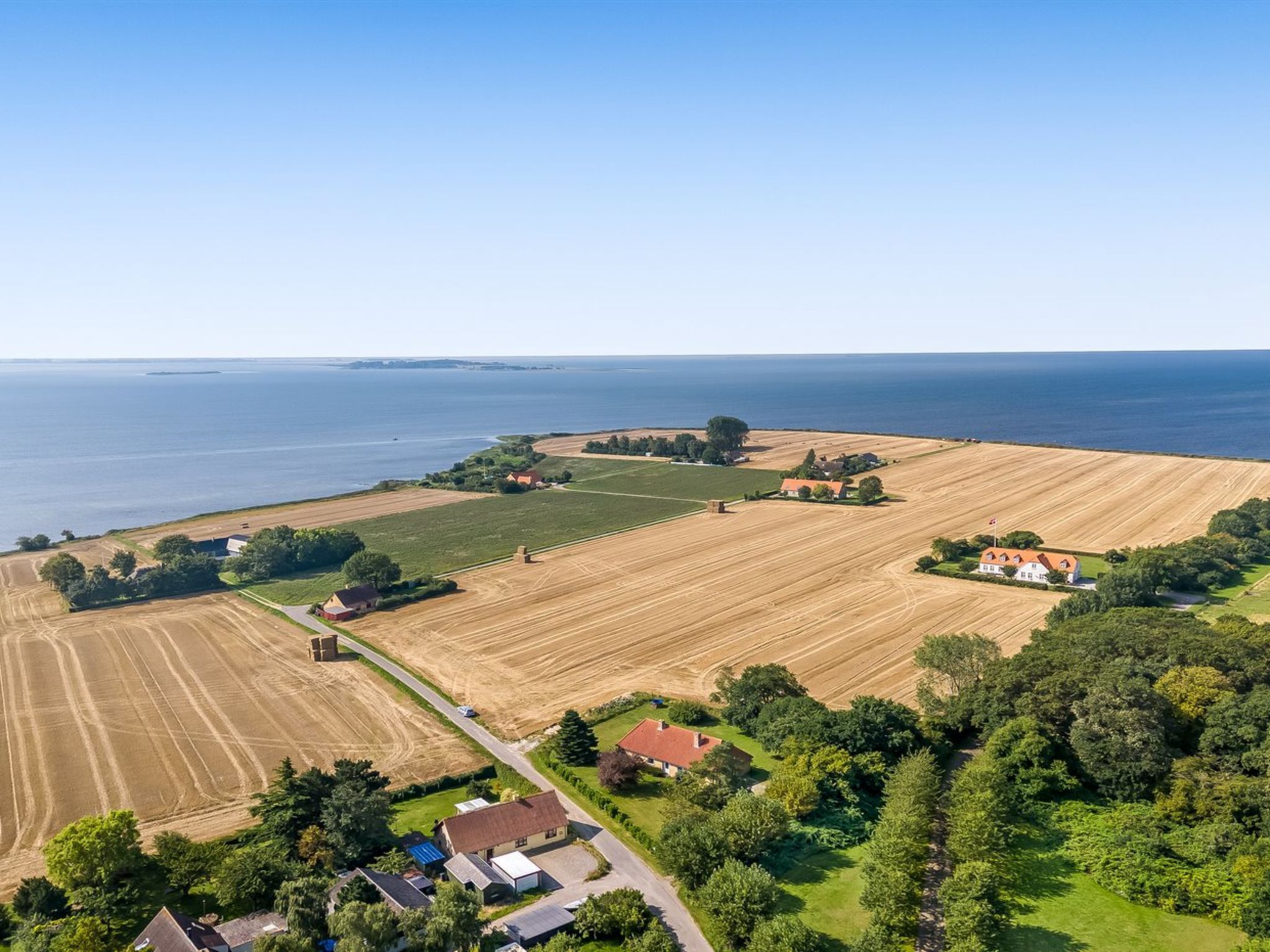 Une vue aérienne d’une zone côtière avec des champs, des maisons et une étendue d’eau.