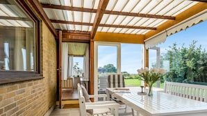 Un patio cubierto con una mesa y sillas, vistas al jardín y un muro de ladrillo.