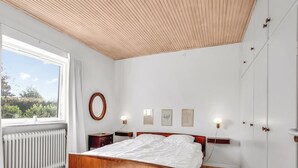 Un dormitorio con cama de madera, espejo redondo, lámparas de noche y vistas a la vegetación exterior.