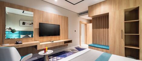 Una habitación de hotel moderna con una cama, un escritorio con silla, un televisor montado en la pared y un armario.