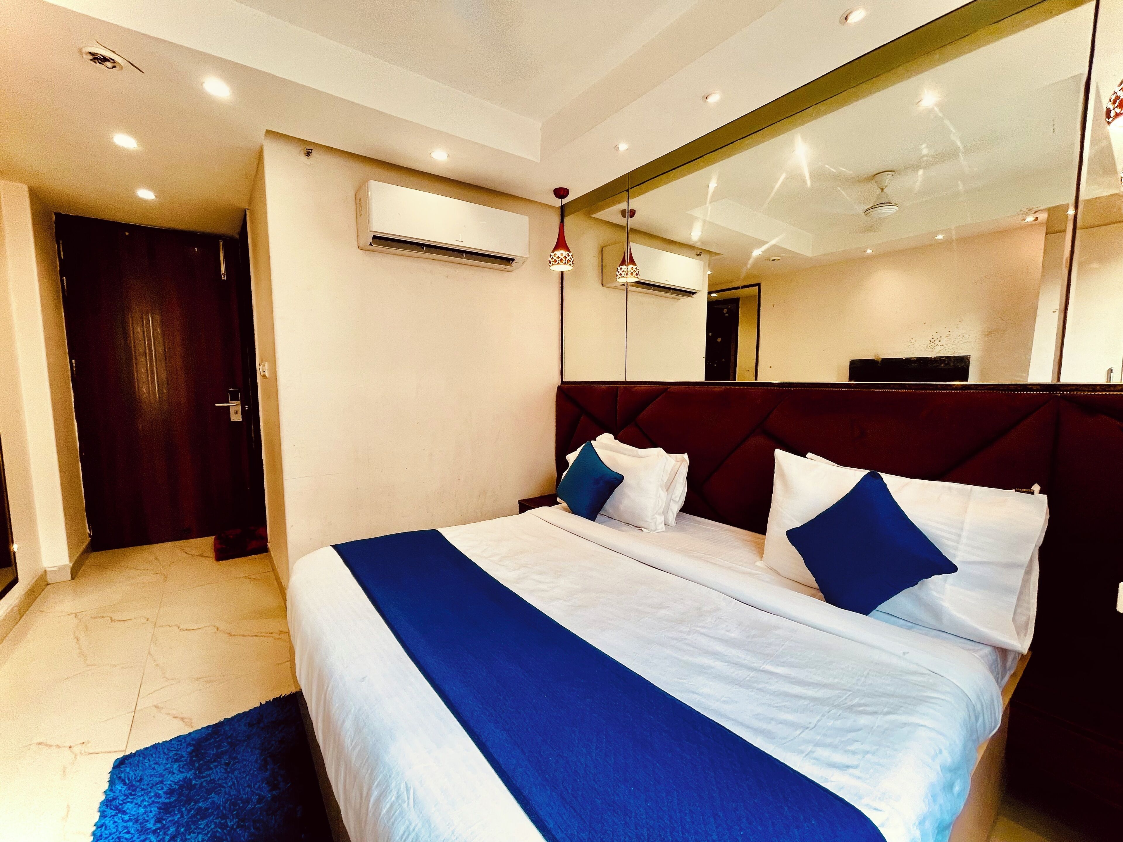 Una camera d'hotel con un letto, uno specchio grande, un condizionatore d'aria e una porta.