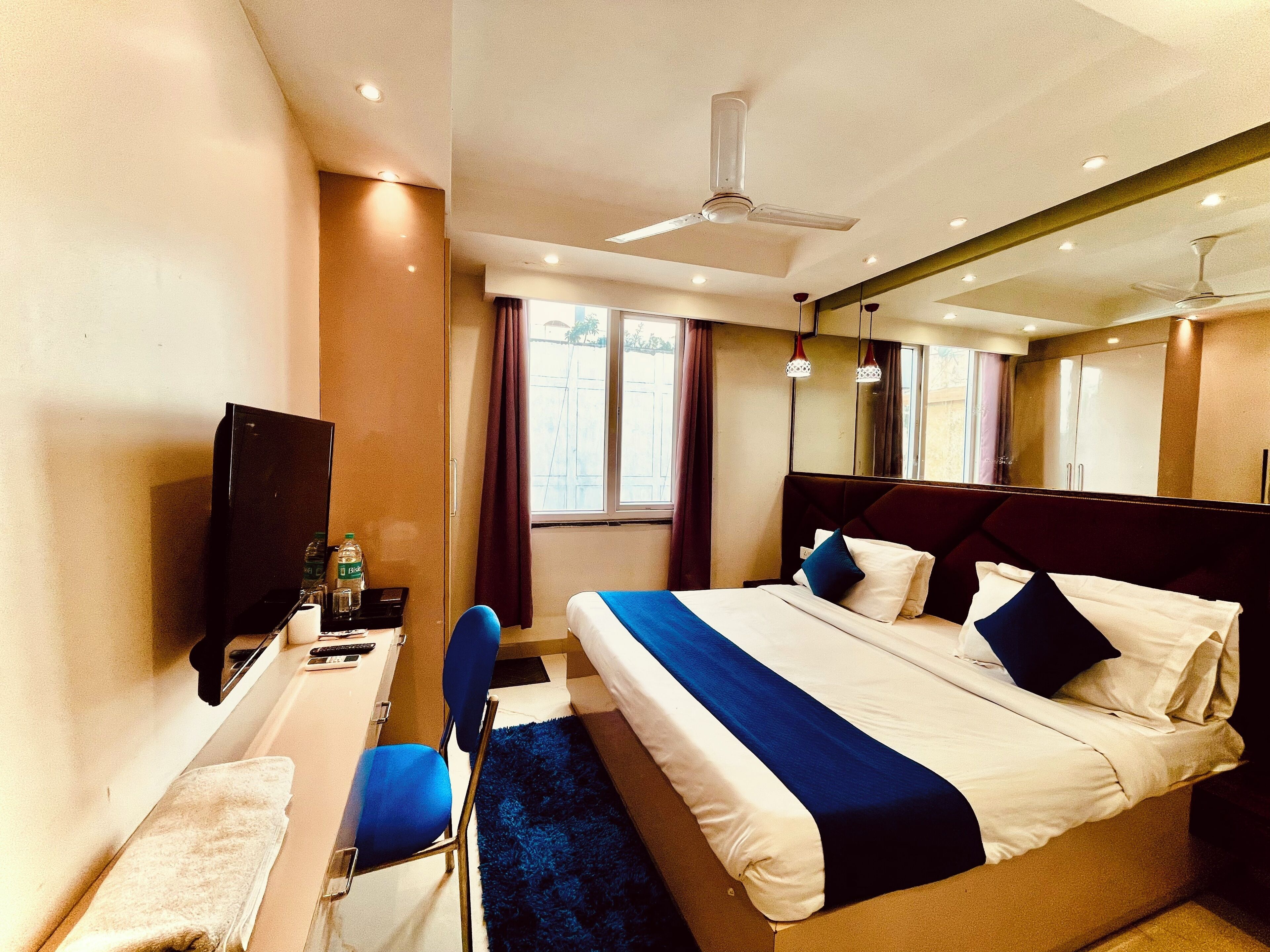 Habitación de hotel con cama, escritorio, silla, televisión y ventana con cortinas.