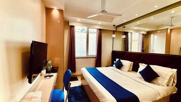 Habitación de hotel con cama, escritorio, silla, televisión y ventana con cortinas.