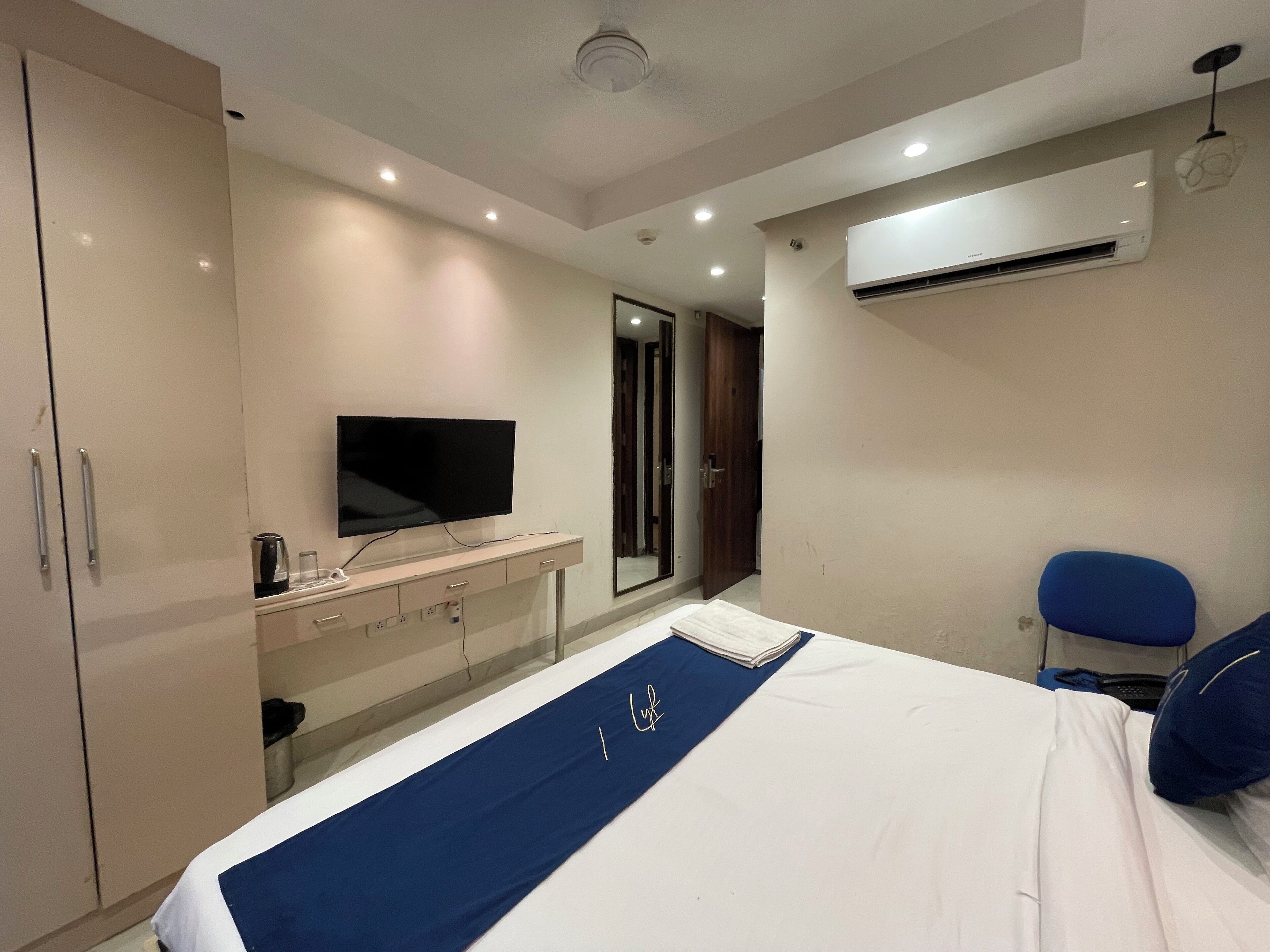 Habitación de hotel con cama, televisor montado en la pared, escritorio con cafetera y unidad de aire acondicionado.
