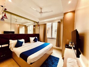 Ein modernes Hotelzimmer mit einem großen Bett, einem Flachbildfernseher, einem Deckenventilator und einem Fenster mit Vorhängen.