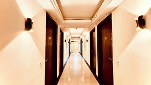 Un couloir d’hôtel avec un sol ciré, des portes sombres et des luminaires fixés au mur.