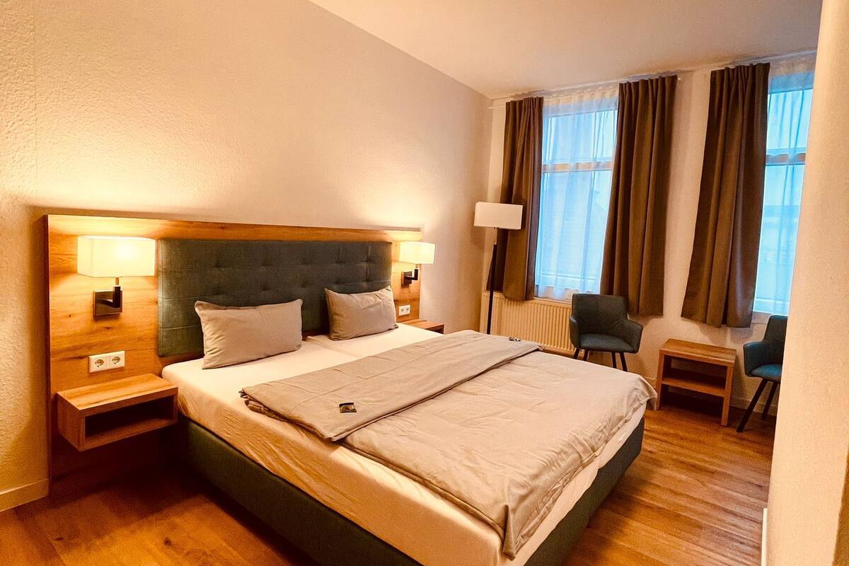 A hotel room with a large bed, bedside lamps, a desk, and a chair.