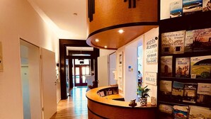 A hotel reception area with a curved desk, a plant, and a wall displaying various brochures. - Haus Borkum (Borkum)
