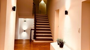 A hallway with wooden flooring, a staircase, a white bench, and a potted plant. - Haus Borkum (Borkum)