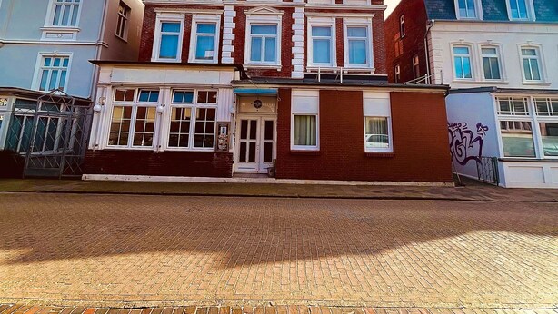 A multi-story building with a brick facade, large windows, and a visible storefront. - Haus Borkum (Borkum)