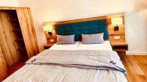 A neatly made bed with a grey duvet, a wooden headboard, and two bedside lamps. - Haus Borkum (Borkum)