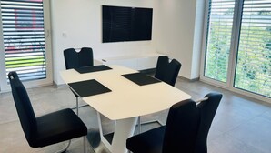 A modern meeting room with a white table, black chairs, and a large black screen on the wall.