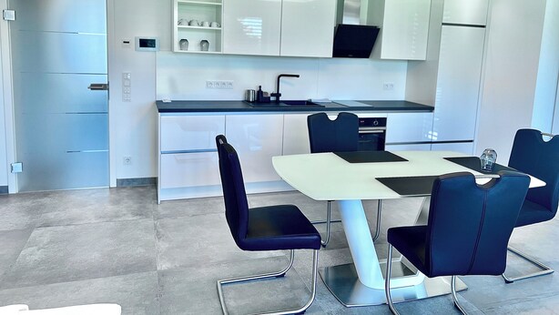A modern kitchen with white cabinets, a black countertop, and a dining area with a white table and black chairs.