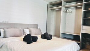 A modern hotel room with a large bed, grey headboard, and a walk-in closet with multiple shelves and a hanging rack.