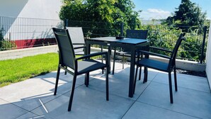 An outdoor patio with a table and chairs, surrounded by a low fence and greenery. - Stylish 1-room apartment + terrace (Herzogenaurach)
