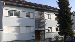 Ein zweistöckiges Wohnhaus mit Ziegeldach, einer Garagentür und einem kleinen Vorgarten mit Baum und Sträuchern.