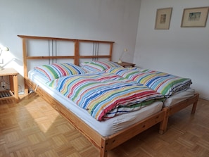 Ein hölzernes Bett mit gestreifter Decke, ein Nachttisch mit Lampe und ein Fußboden mit Fischgrätmuster.