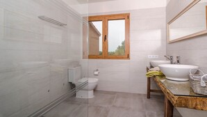 A modern bathroom with a glass shower enclosure, a toilet, a sink with a wooden countertop, and a window with a wooden frame. - Can Xesquet - Villa With Private Pool. Free Wifi (Ses Salines, Illes Balears)