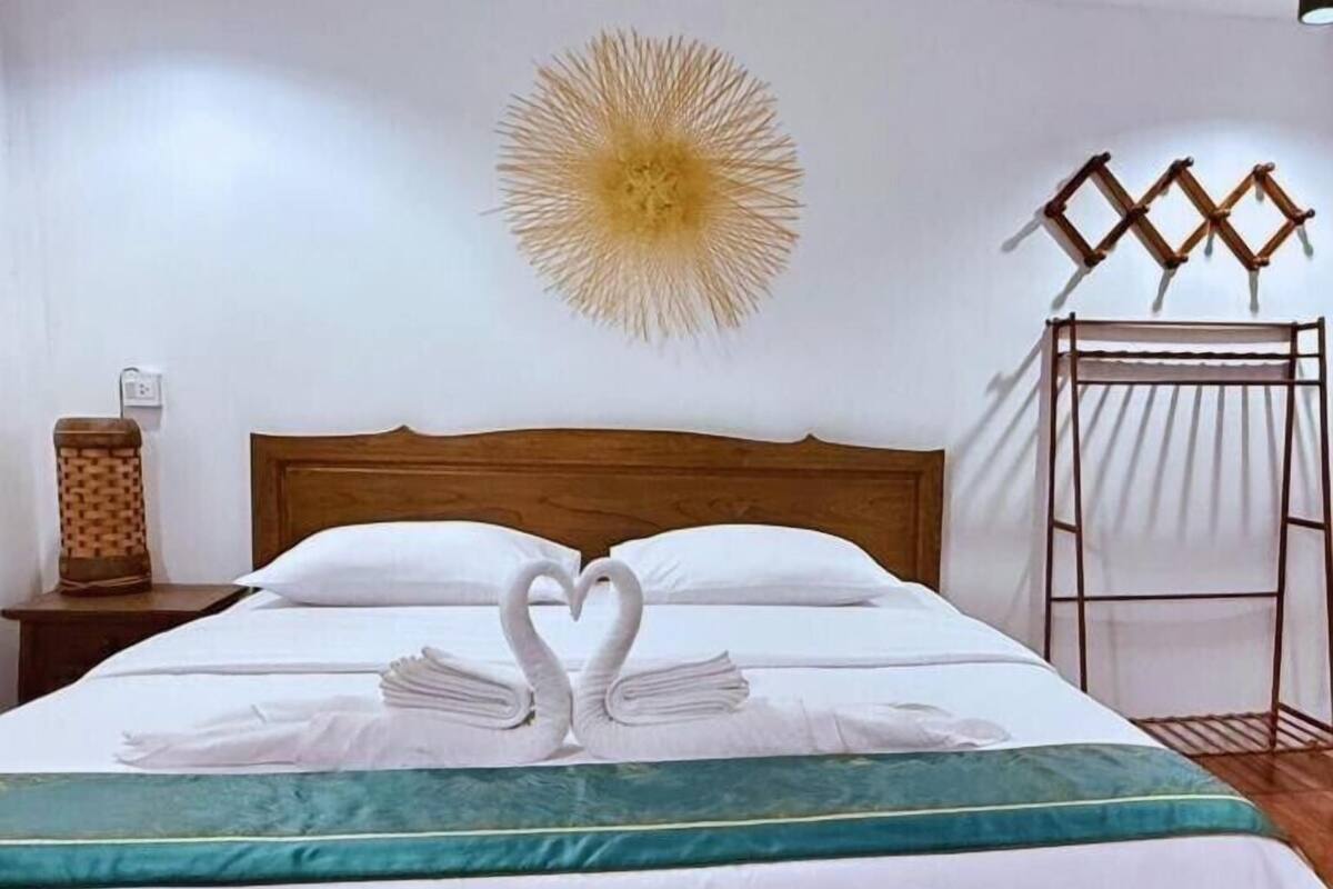 A neatly made bed with white linens and two towels arranged in a heart shape.