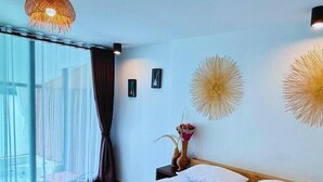 Camera d'albergo con un letto grande, una testiera in legno, una finestra con tende leggere e luci decorative a parete.