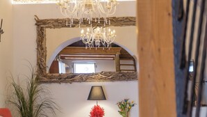 Une pièce dotée d’un miroir rustique à cadre en bois, d’un lustre, d’une lampe et donnant sur un escalier en bois.