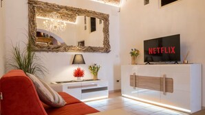 Un salon moderne avec un grand miroir, un téléviseur à écran plat affichant le logo « NETFLIX », un canapé rouge, une console blanche et un meuble en bois.