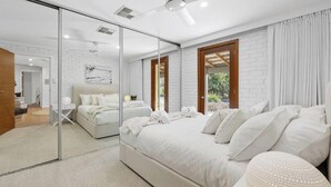 A bedroom with a large bed, a mirror, and a view of the outdoors. - Reflections in the Sea by Wine Coast Holidays (ALDINGA BEACH)