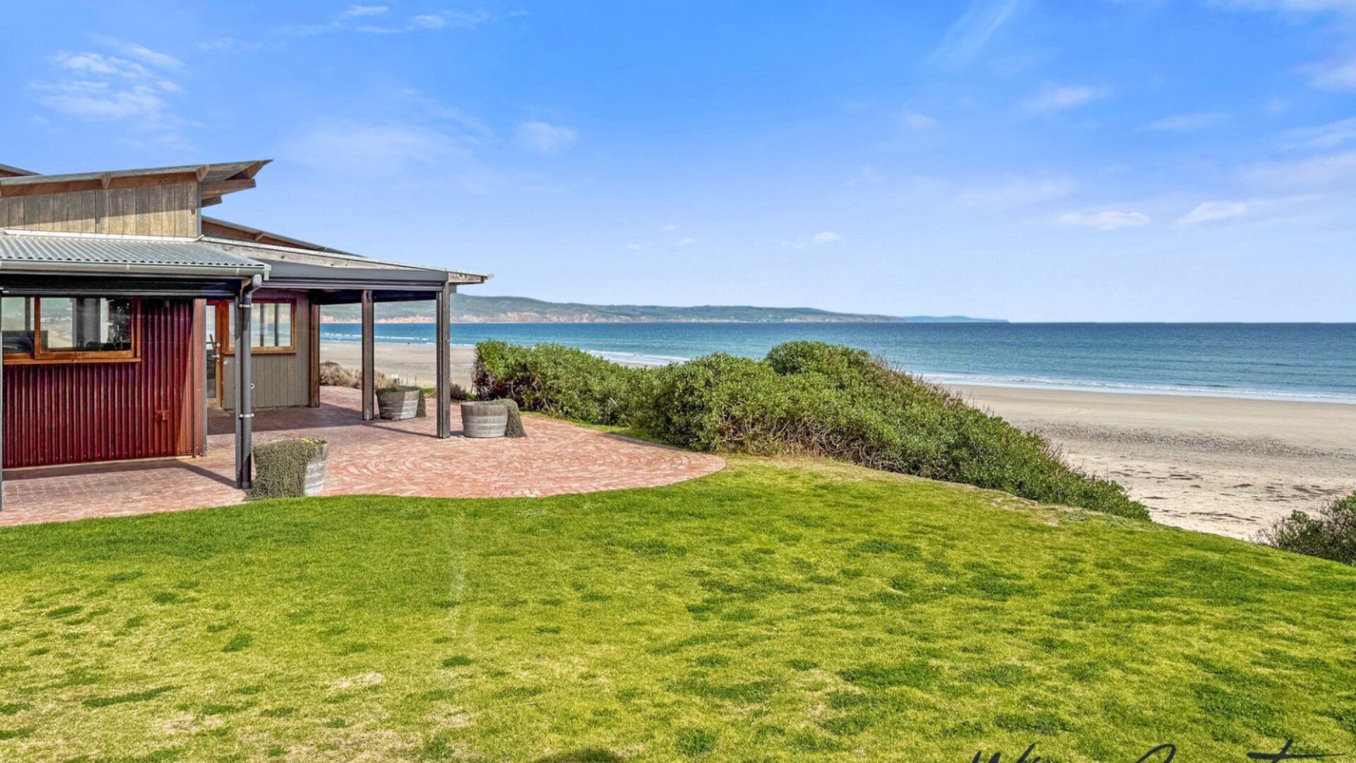 A coastal property with a covered patio, a grassy lawn, and a view of the beach and ocean. - Reflections in the Sea by Wine Coast Holidays (ALDINGA BEACH)