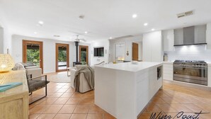 A modern kitchen with a large island, built-in oven, and a dining area with a sofa and table. - Reflections in the Sea by Wine Coast Holidays (ALDINGA BEACH)