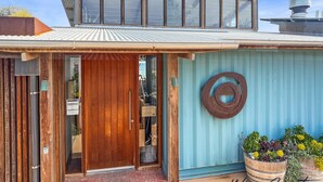 A modern house with a wooden door, a blue exterior wall, and a metal roof. - Reflections in the Sea by Wine Coast Holidays (ALDINGA BEACH)
