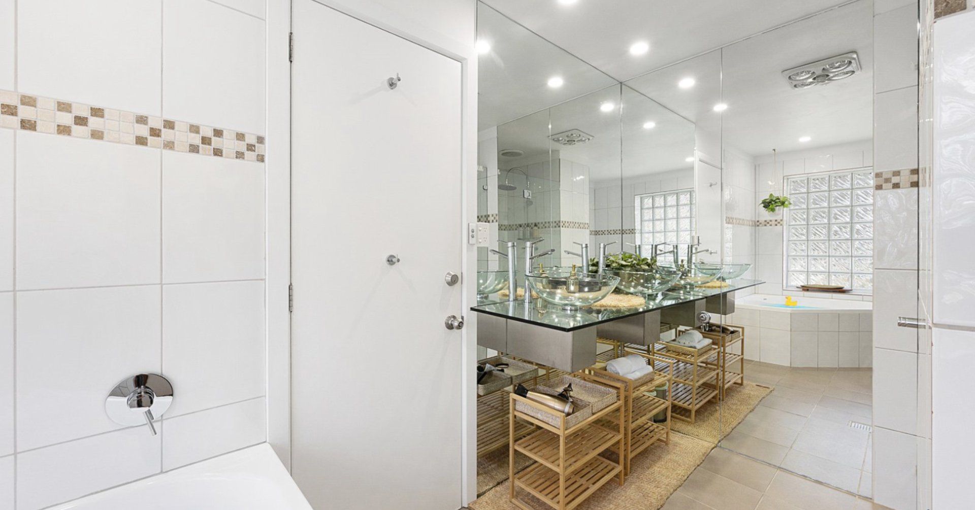 A modern bathroom with a glass-enclosed sink, a bathtub, and a large mirror.