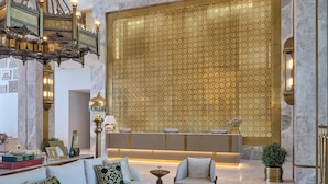 Un hall d’entrée luxueux, doté d’un plafond haut, de lustres somptueux, d’un comptoir de réception et d’un espace salon avec un canapé et des fauteuils.