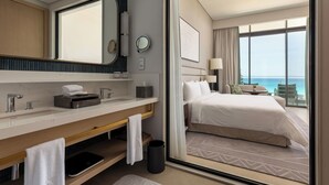 Une chambre d’hôtel avec un grand lit, une salle de bain équipée d’un lavabo, d’un miroir et offrant une vue sur l’océan.