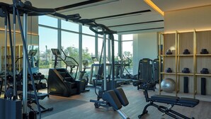 A modern gym with various exercise equipment, large windows, and a view of palm trees. - Palace Beach Resort (El Alamein)