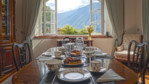 Une salle à manger avec une table mise pour le petit-déjeuner, une vue sur les montagnes par une grande fenêtre et un fauteuil ancien.
