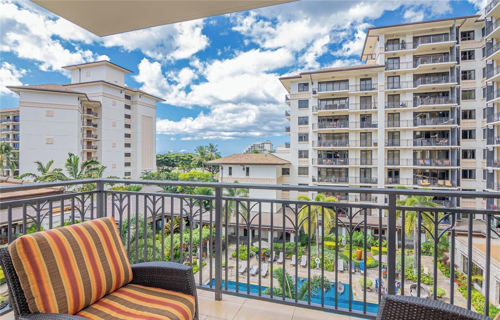A balcony with wicker furniture, a pool, and high-rise buildings in the background.