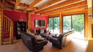 Un salón amplio con techo de madera, una pared de acento roja, un televisor grande y un ventanal corredizo que da a un balcón.
