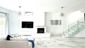 A modern living room with a marble floor, a sofa, a fireplace, and a staircase.