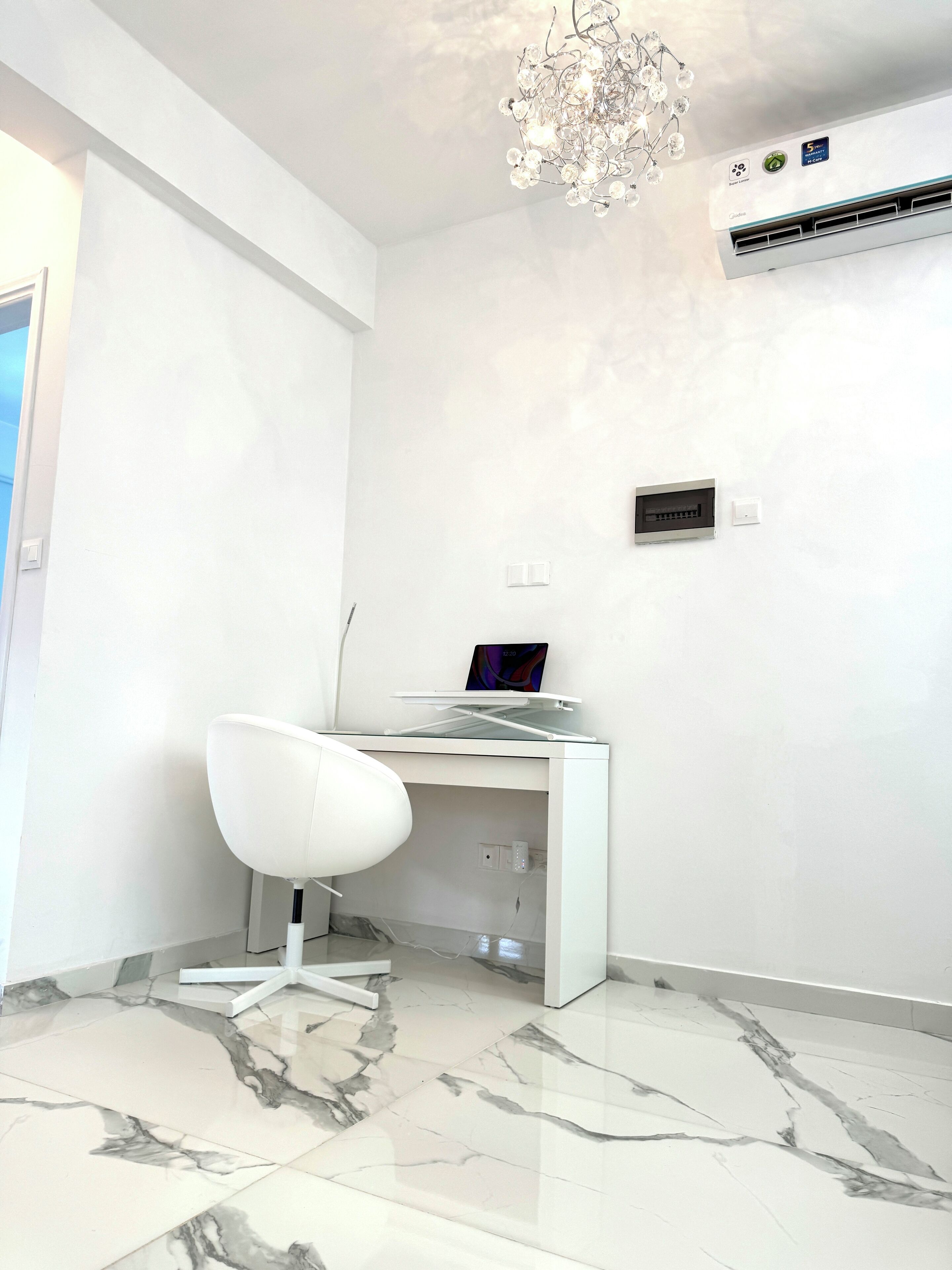 A modern room with a white desk, a white chair, a laptop, and a chandelier.