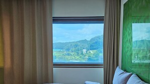 Quarto com uma cama grande, janela com vista para uma paisagem verde e parede verde.