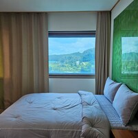 Quarto com uma cama grande, janela com vista para uma paisagem verde e parede verde.