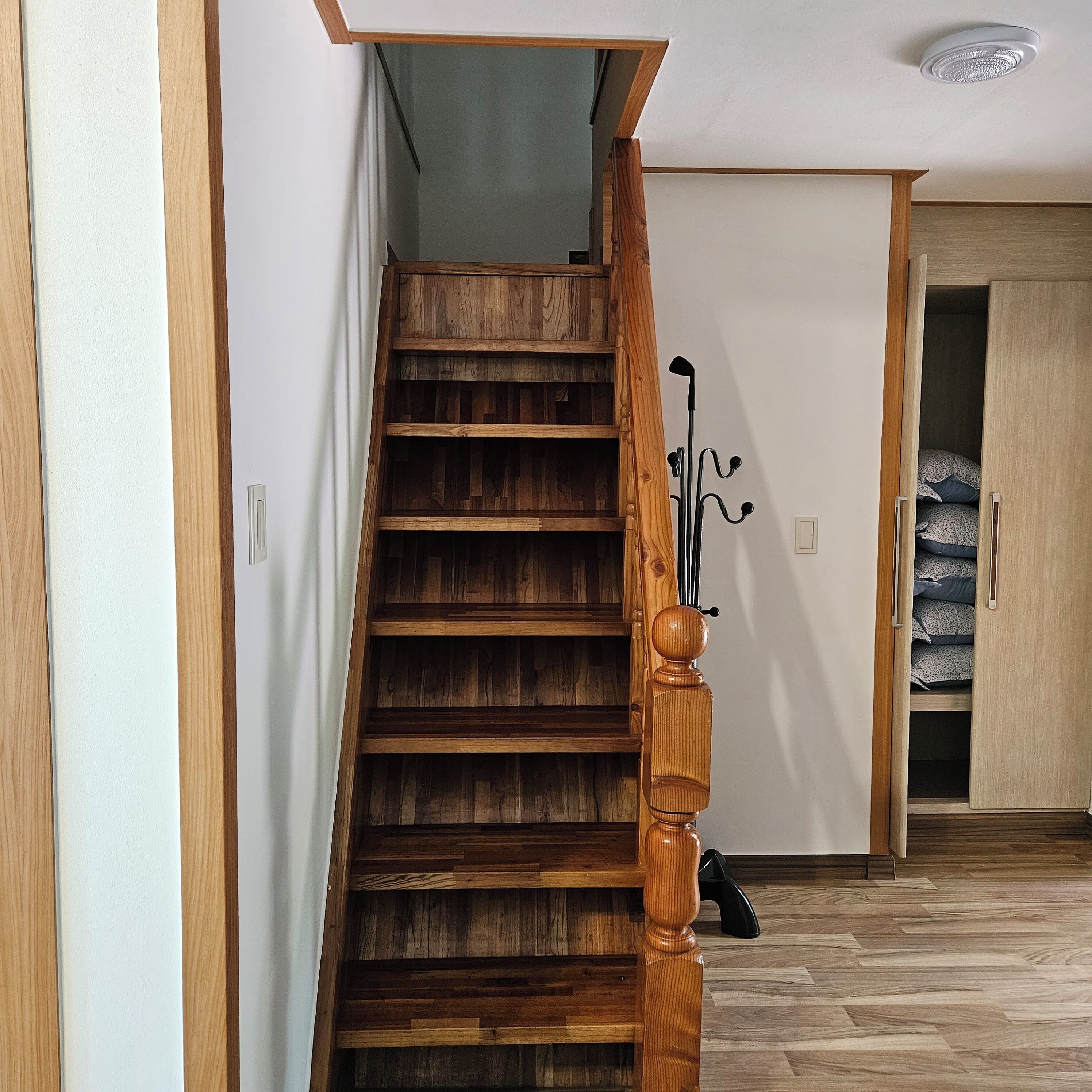 Een houten trap met een leuning, die leidt naar een kamer met een kledingkast en een bed.