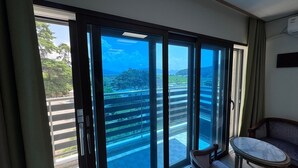 Quarto com porta de vidro deslizante para uma varanda com vista para uma paisagem verde e um céu azul claro.