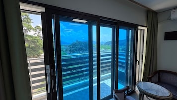Quarto com porta de vidro deslizante para uma varanda com vista para uma paisagem verde e um céu azul claro.